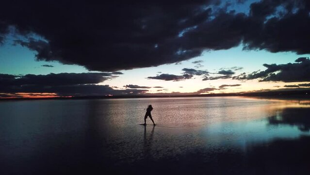 young woman dance across the mirror like surface of salt lake as the sun disappears behind the clouds.