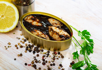 Can of preserves with whole stuffed squid in ink on light wooden background