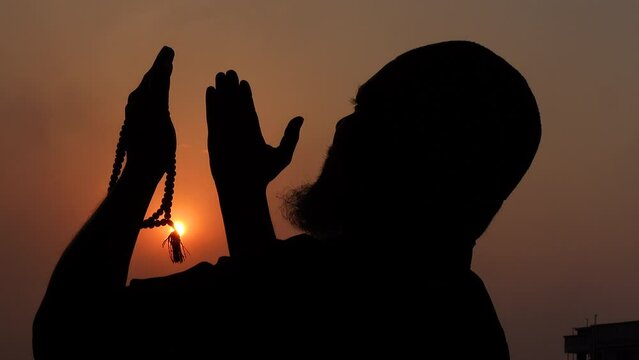 A Muslim old man praying with his hands raised to the sky in the afternoon twilight.