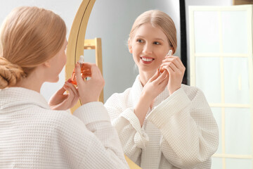 Obraz na płótnie Canvas Young blonde woman with facial serum near mirror in bathroom