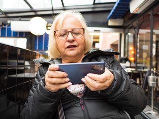 gamer grandmother playing on the mobile phone on a restaurant terrace - 780151027