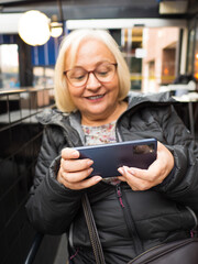 Defocused blonde gamer grandmother playing on smartphone - 780151452
