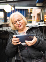 Defocused blonde gamer grandma concentrated playing on smartphone - 780151680