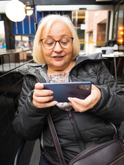 Blonde gamer grandmother is surprised playing on smartphone - 780151898