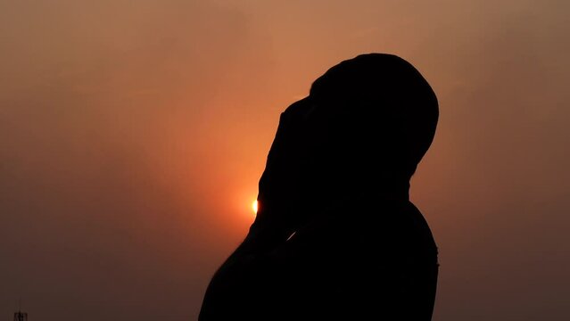 A Muslim old man praying with his hands raised to the sky in the afternoon twilight.