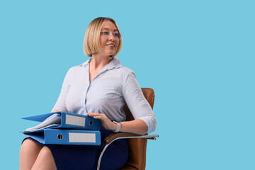 Mature businesswoman with office folders sitting on chair against blue background