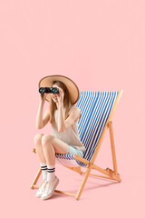 Female tourist looking through binoculars in deck chair on pink background