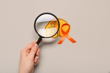 Female hand with magnifying glass, paper brain and orange ribbon on grey background. Multiple Sclerosis Awareness Month