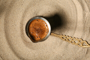 Cezve of hot coffee on sand background