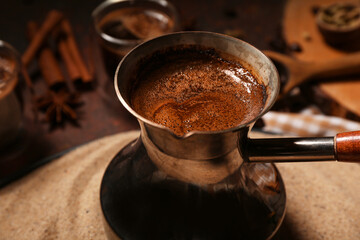 Fototapeta premium Cezve of delicious Turkish coffee in sand on dark background