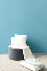 Soft pillows with plaid on pouf near blue wall in room