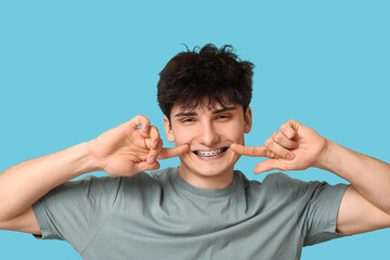Smiling young man with dental braces on blue background