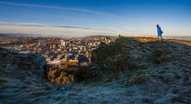 A young man in a blue coat takes in a panoramic view from Arthur's Seat, a volcanic peak overlooking Edinburgh, Scotland.
