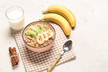 Bowl with tasty oatmeal, bananas, kiwi and glass of milk on light background