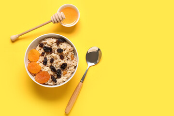 Bowl with tasty oatmeal, dried fruits and honey on yellow background