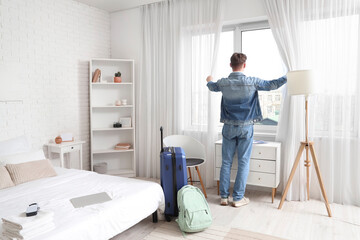 Male tourist opening curtains in hotel room, back view