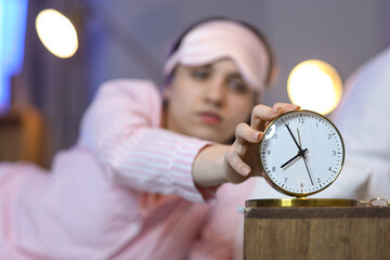 Young woman turning off alarm clock in bedroom at night, closeup