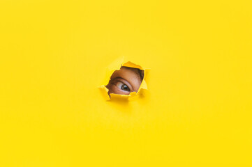 Left eye looking through a hole in a yellow paper. Voyeurism. The man is watching the wife. A...