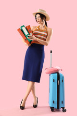 Young businesswoman with folders and suitcase ready for summer vacation on pink background