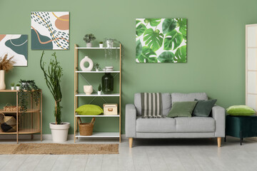 Interior of living room with comfortable sofa, olive pillows and houseplants near green wall