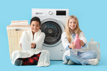 Children with bottles of laundry detergent sitting near washing machine against blue background