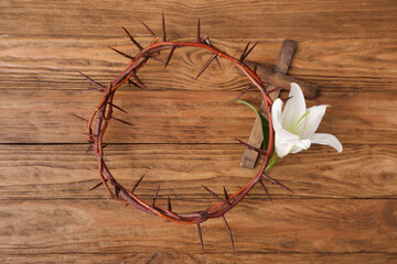 Crown of thorns with white lily and cross on wooden background