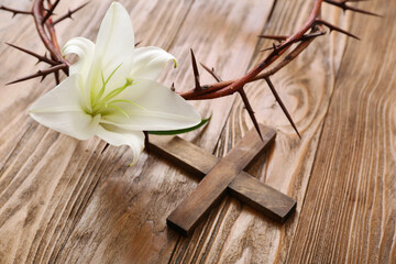 White lily, crown of thorns and cross on wooden background, closeup