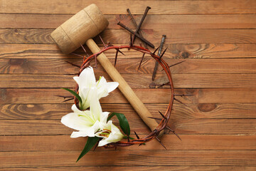 Crown of thorns with white lilies, hammer and nails on wooden background