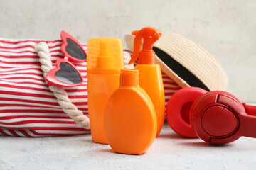 Composition with bottles of sunscreen cream, headphones, bag, sunglasses and hat on white table near light wall