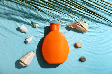 Bottle of sunscreen cream and seashells in water on blue background