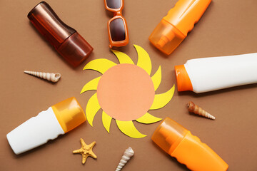 Paper sun figure, seashells, sunglasses and bottles of sunscreen cream on brown background