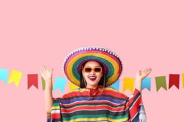 Happy young woman in Mexican sombrero hat and poncho on pink background