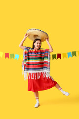 Happy young woman in Mexican sombrero hat and poncho on yellow background