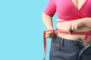 Overweight woman measuring waist on blue background, closeup. Diet concept