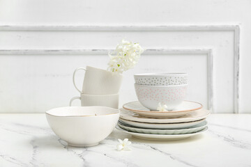 Beautiful tableware with flowers on marble table near white wall