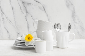 Beautiful tableware with daffodil on white table near marble wall