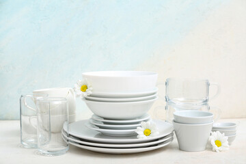 Composition with clean dishes, cups, glasses and beautiful chamomiles on table near light wall