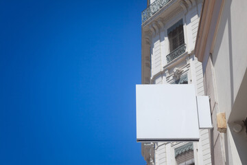 Selective blur on a Empty white square shop signboard hanging on a building facade, visible against a clear sky in a French city street ideal for retail business advertising & urban commercial display