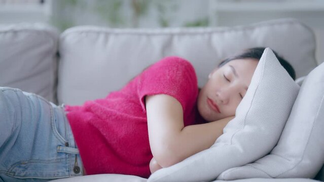 Asian woman resting at home on couch, feeling exhausted after work, lacking energy, or overworked, too tired, and lacking motivation