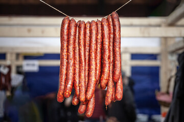 Selective blur on cajna kobasica sausages spiked for sale hanging on a stand of a serbian market. Cajna kobasica, or tea sausage, is a traditional serbian sausage made of smoked cured pork.