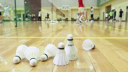 体育館の床にあるバドミントンのシャトルと運動する人々の姿
