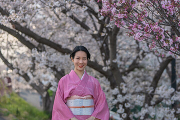満開の桜を背景に、着物を着た若い女性の笑顔のポートレート