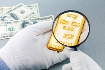 Hand holding magnifying glass with gold bar Financial concept