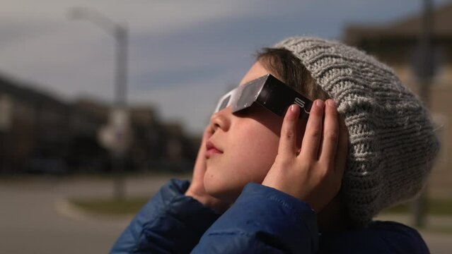 Boy puts on solar glasses and looks up to watch eclipse - side profile