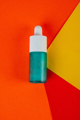 Blue glass cosmetic bottle, Skin care or sunscreen cosmetic on red and orange and yellow background.