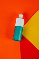 Blue glass cosmetic bottle, Skin care or sunscreen cosmetic on red and orange and yellow background.