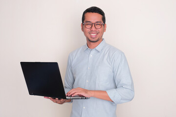 Adult Asian man smiling at the camera while holding a laptop