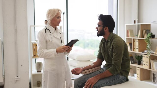 Efficient general practitioner checking solution for chemotherapy of male sitting on exam couch. Young bearded man in casual wear taking dropper while mature female making system review.