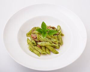 Penne pesto sauce with ham and bacon top with basil leaves served on white plate isolated on white background.