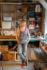 Pleased thoughtful woodworker woman take break in carpentry workshop smiling looking to window...
